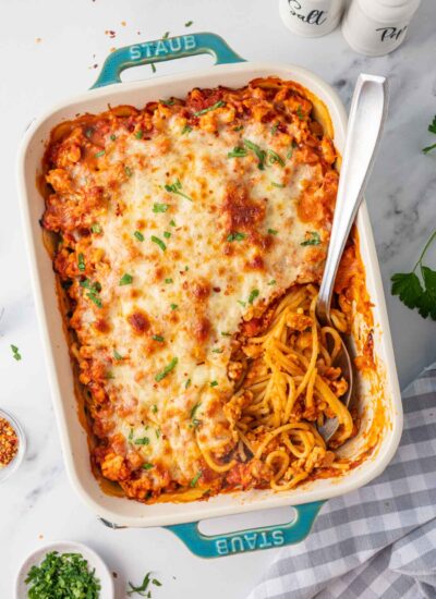 A spoon rests in a casserole dish of million dollar spaghetti.