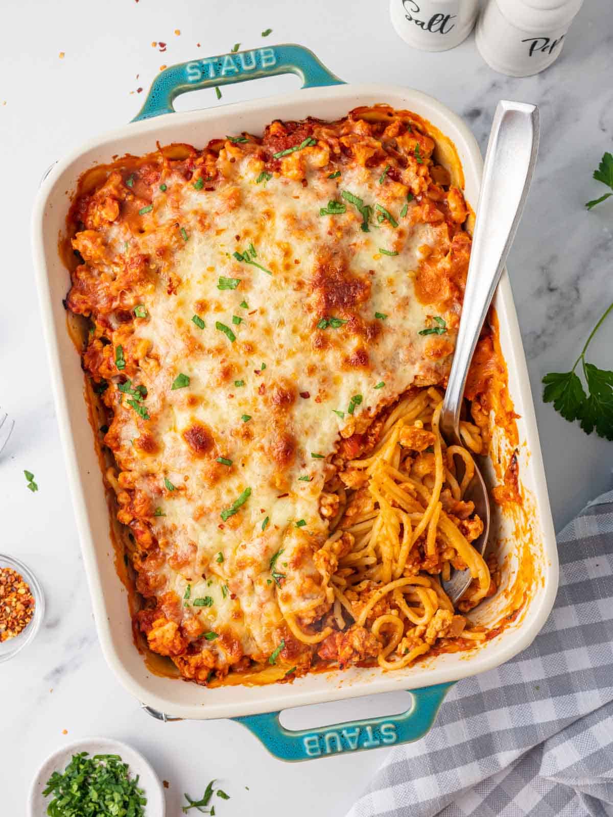 A spoon rests in a casserole dish of million dollar spaghetti.