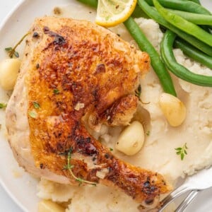 Braised chicken quarter on a plate with mashed potatoes.