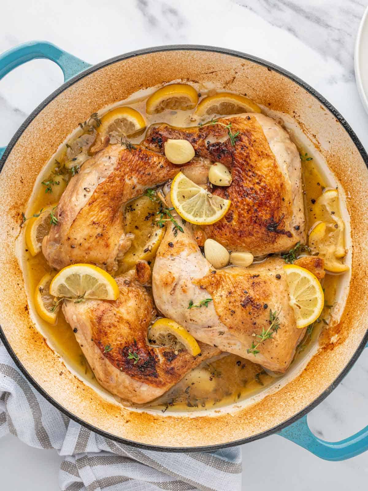 Braised chicken leg quarters with lemon and garlic in a dutch oven.
