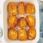 Golden Parmesan-crusted potato halves garnished with parsley in a ceramic baking dish.