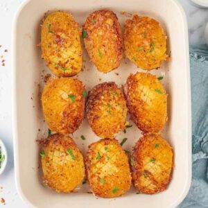 Golden Parmesan-crusted potato halves garnished with parsley in a ceramic baking dish.