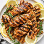 Juicy chicken tenderloins with charred grill marks, a glossy mustard glaze, and chopped parsley on a white serving plate.