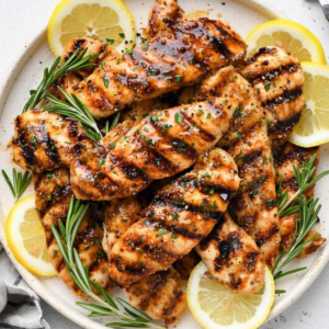 Juicy chicken tenderloins with charred grill marks, a glossy mustard glaze, and chopped parsley on a white serving plate.