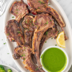 Cooked lamb chops arranged on a platter with parsley-mint sauce and lemon wedges.