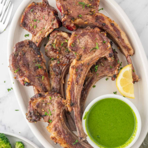 Cooked lamb chops arranged on a platter with parsley-mint sauce and lemon wedges.