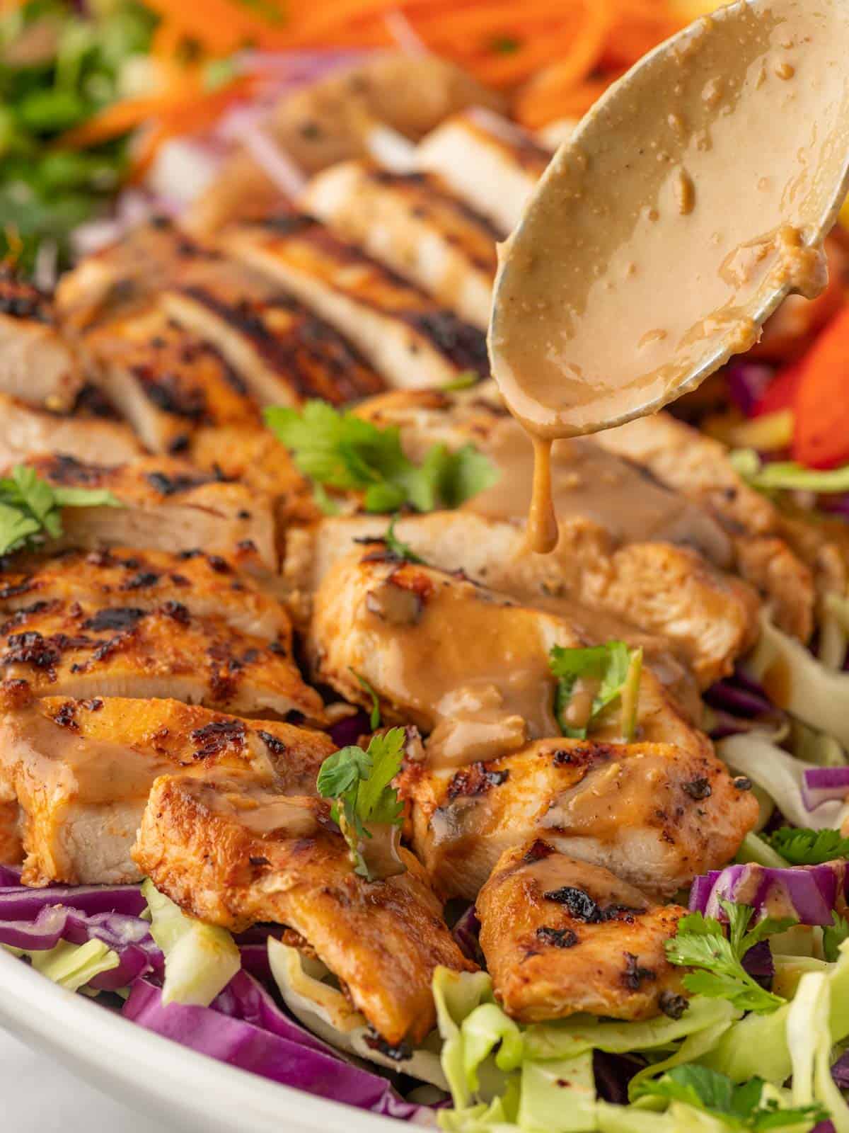 A spoon drizzles peanut butter over grilled chicken.