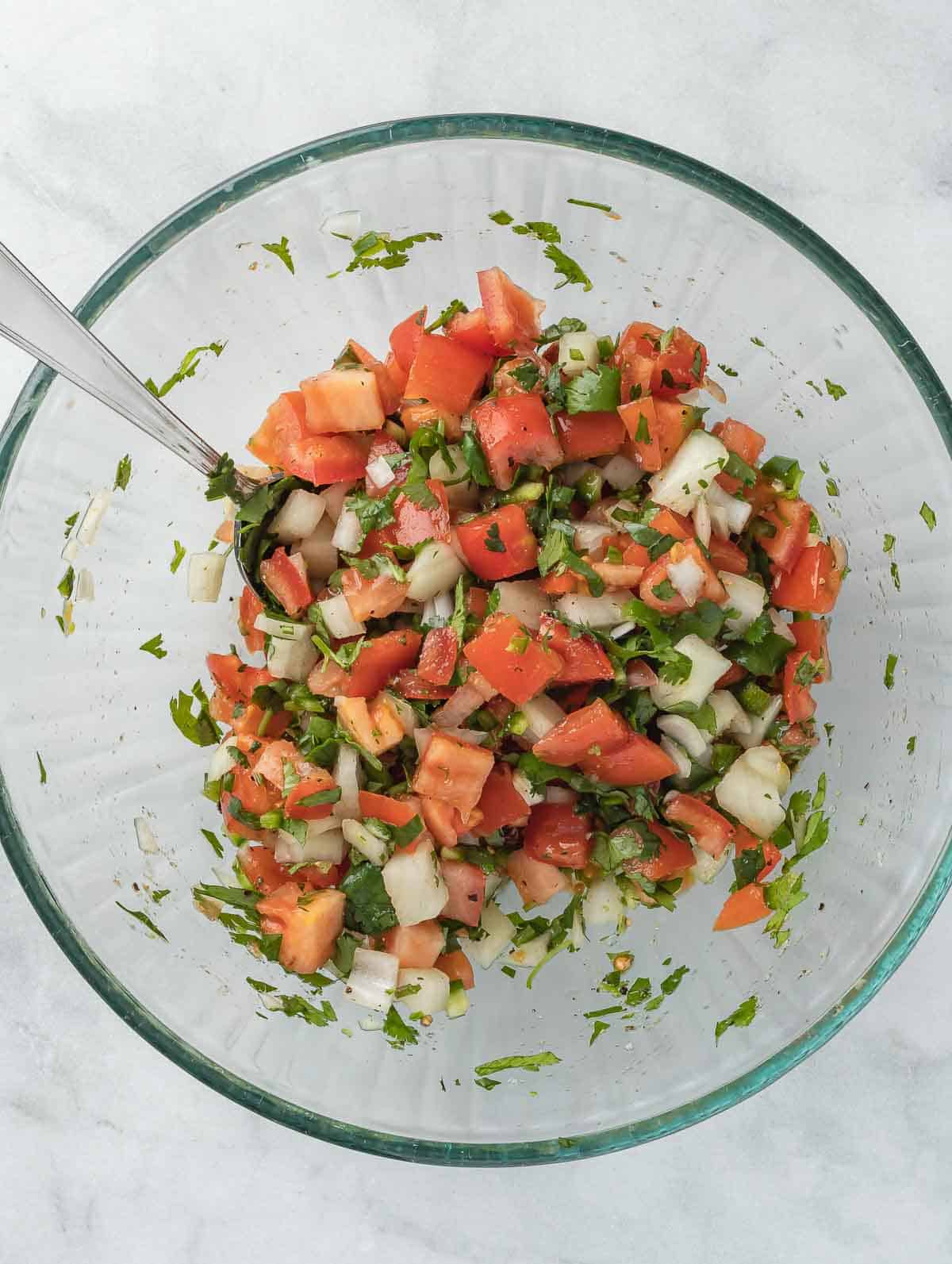 pico de gallo in a clear bowl after mixing ingredients.