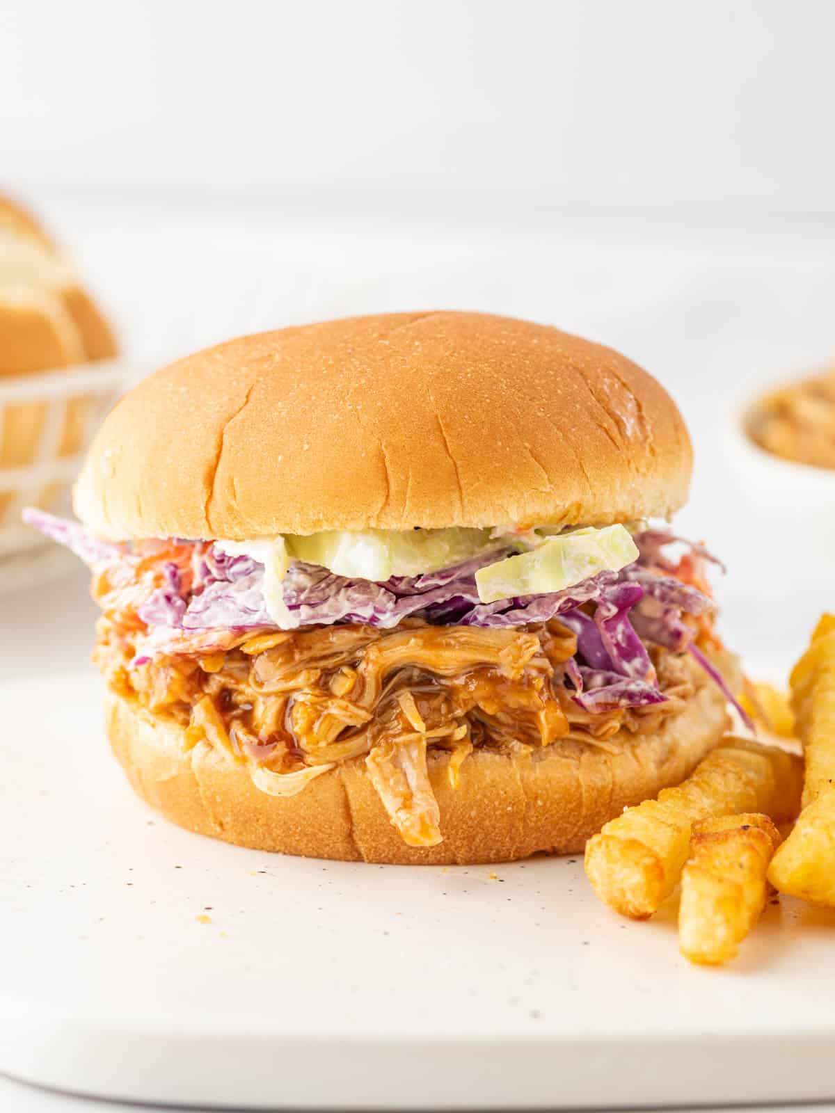 A bbq pulled chicken sandwich on a plate with french fries.