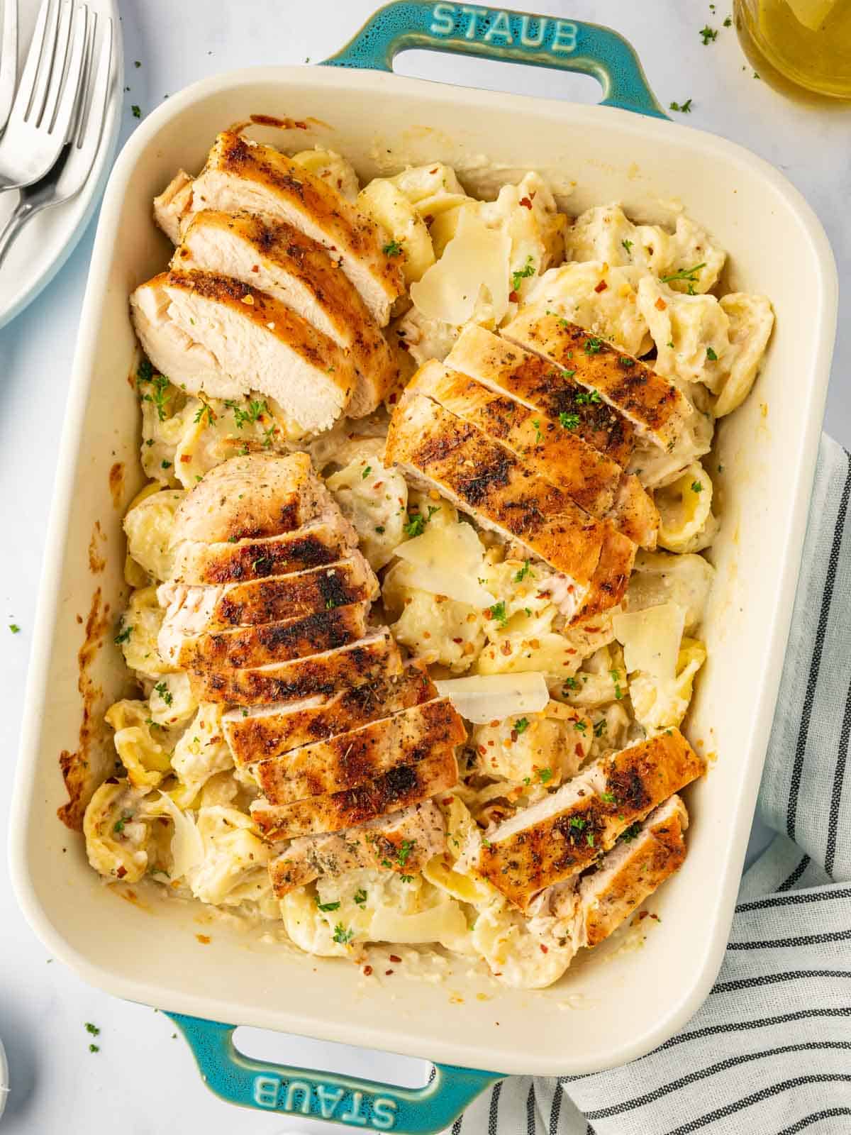 A baking dish with alfredo tortellini and sliced grilled chicken.