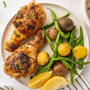 BBQ chicken legs on a plate with veggies and lemon wedges.