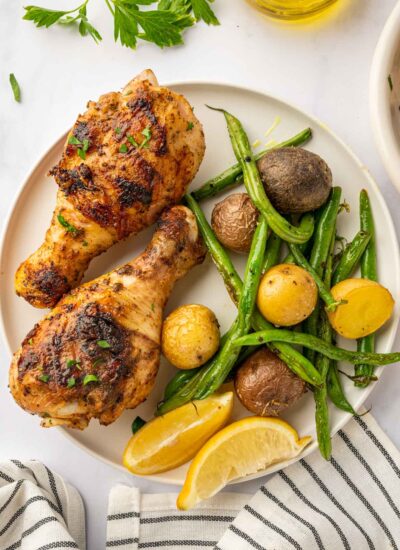 BBQ chicken legs on a plate with veggies and lemon wedges.