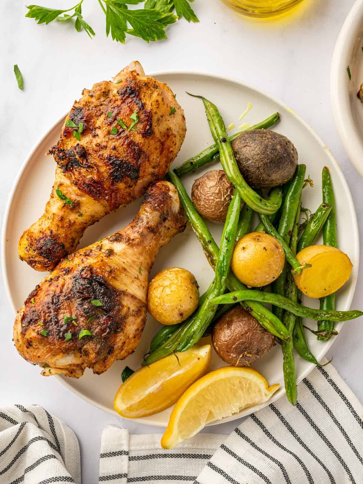 BBQ chicken legs on a plate with veggies and lemon wedges.