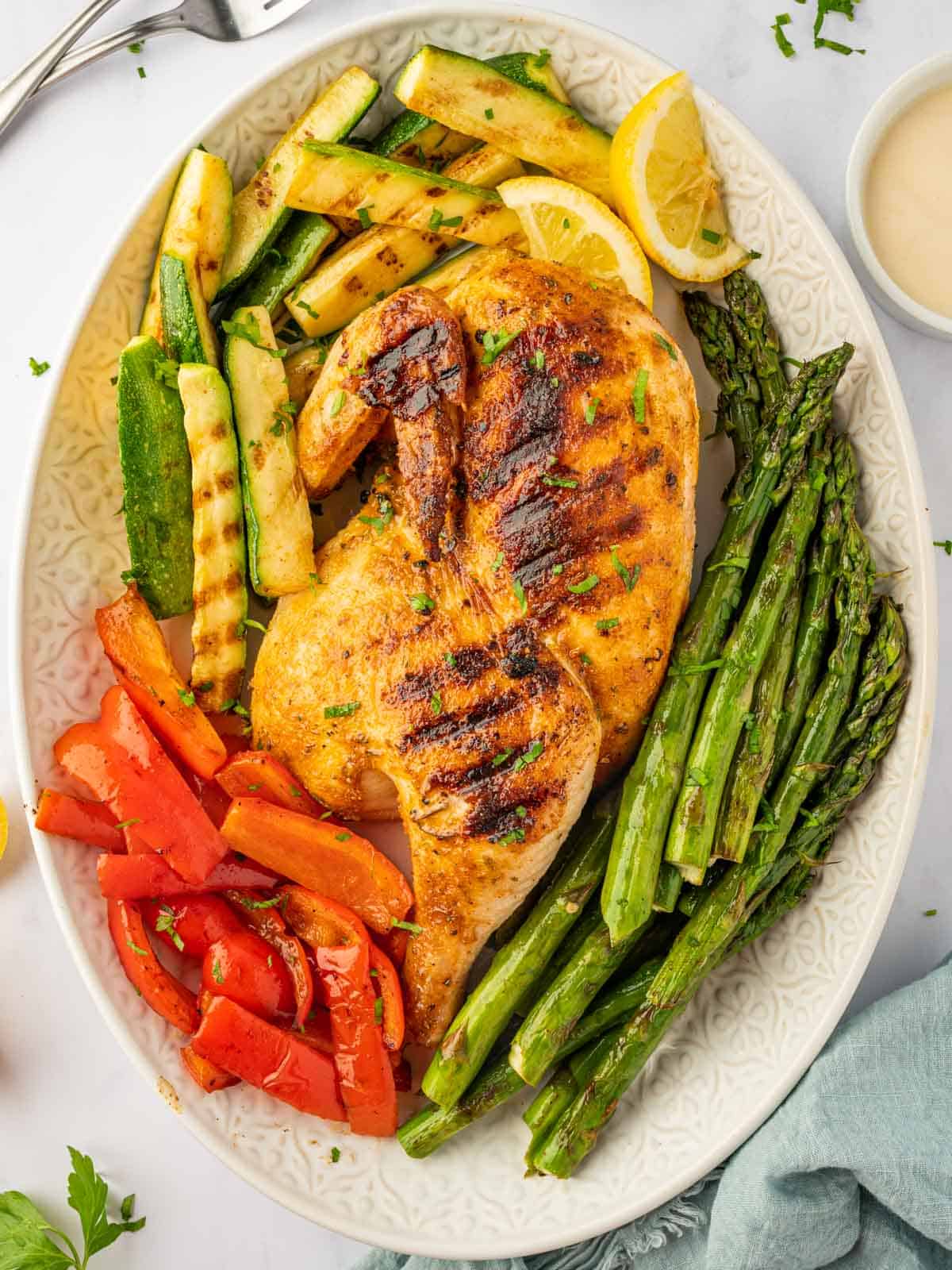 Grilled half chicken on a platter with grilled veggies.