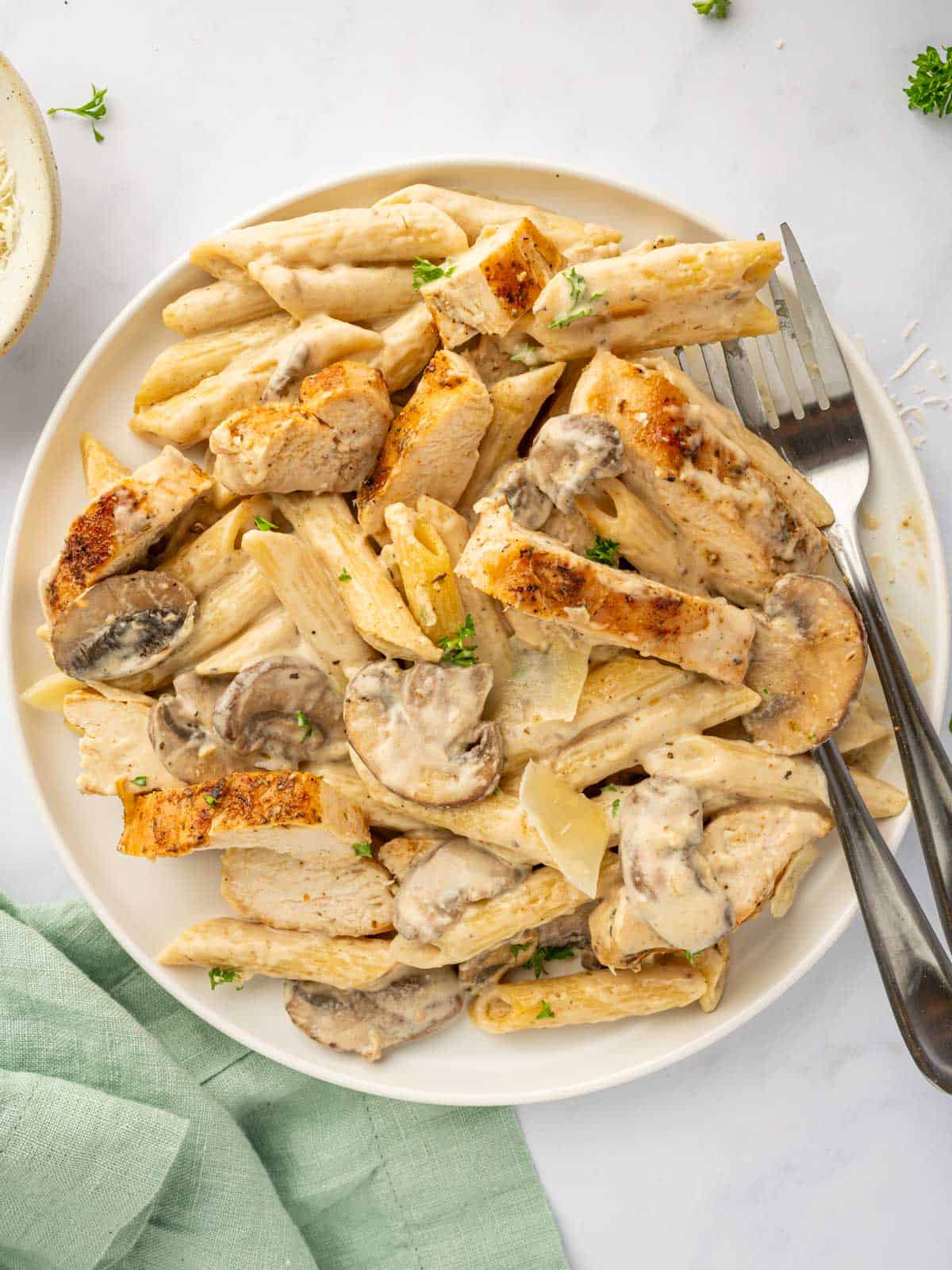 A fork rests on a plate of chicken parmesan garlic pasta.