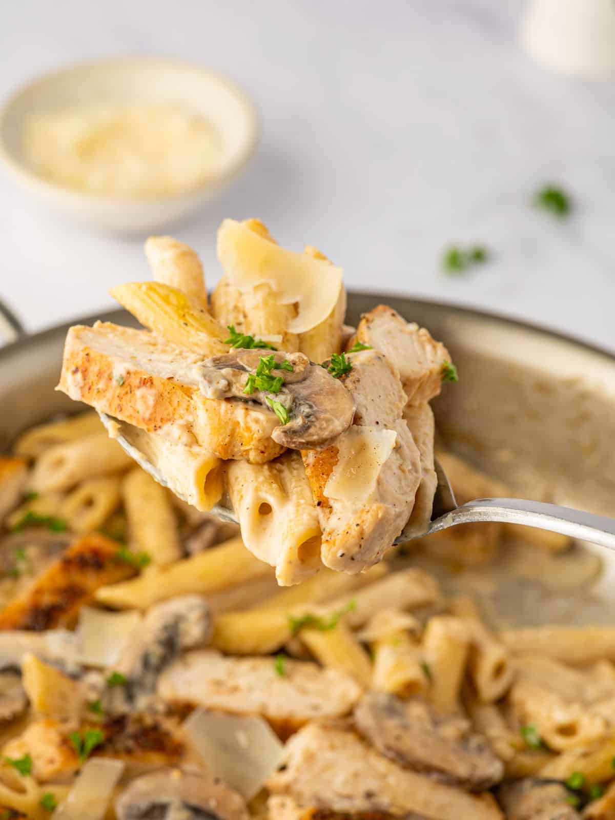 A spoon lifts a bite of creamy chicken and mushroom pasta.