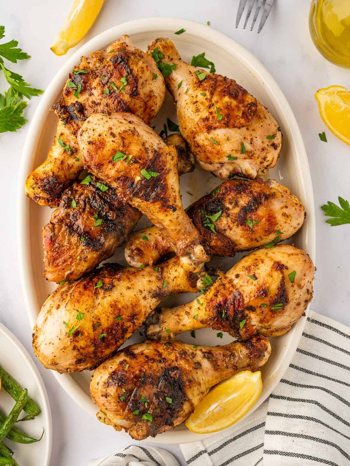 A platter with grilled chicken legs garnished with lemon wedges.