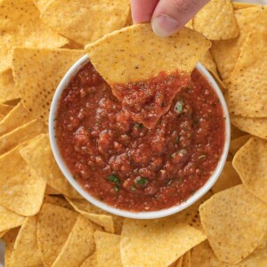 salsa and chips on a plate and hand holding a chip.