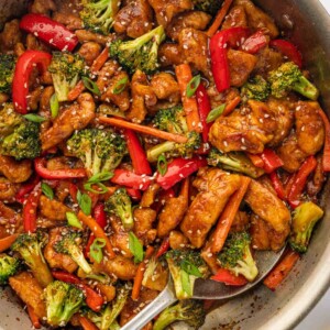 A spoon serve spicy hunan chicken from a skillet.