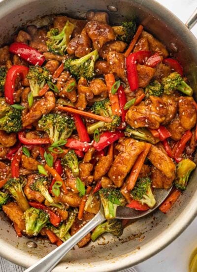 A spoon serve spicy hunan chicken from a skillet.