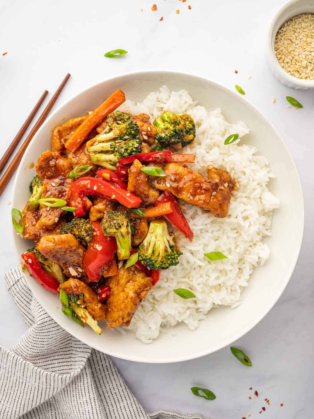 Chinese hunan chicken served over rice with chopsticks.