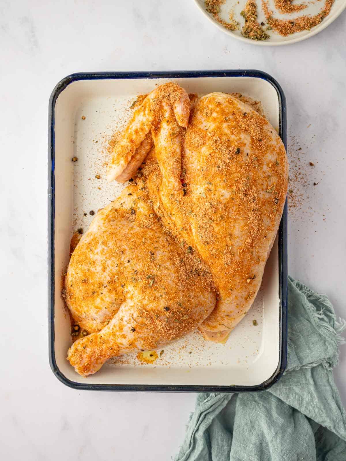 A half chicken is seasoned with herbs and spices.