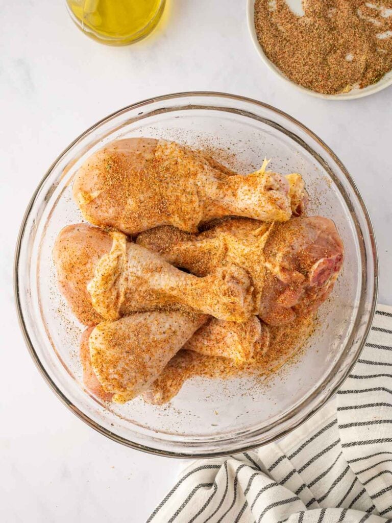 Chicken legs in a bowl sprinkled with seasoning.