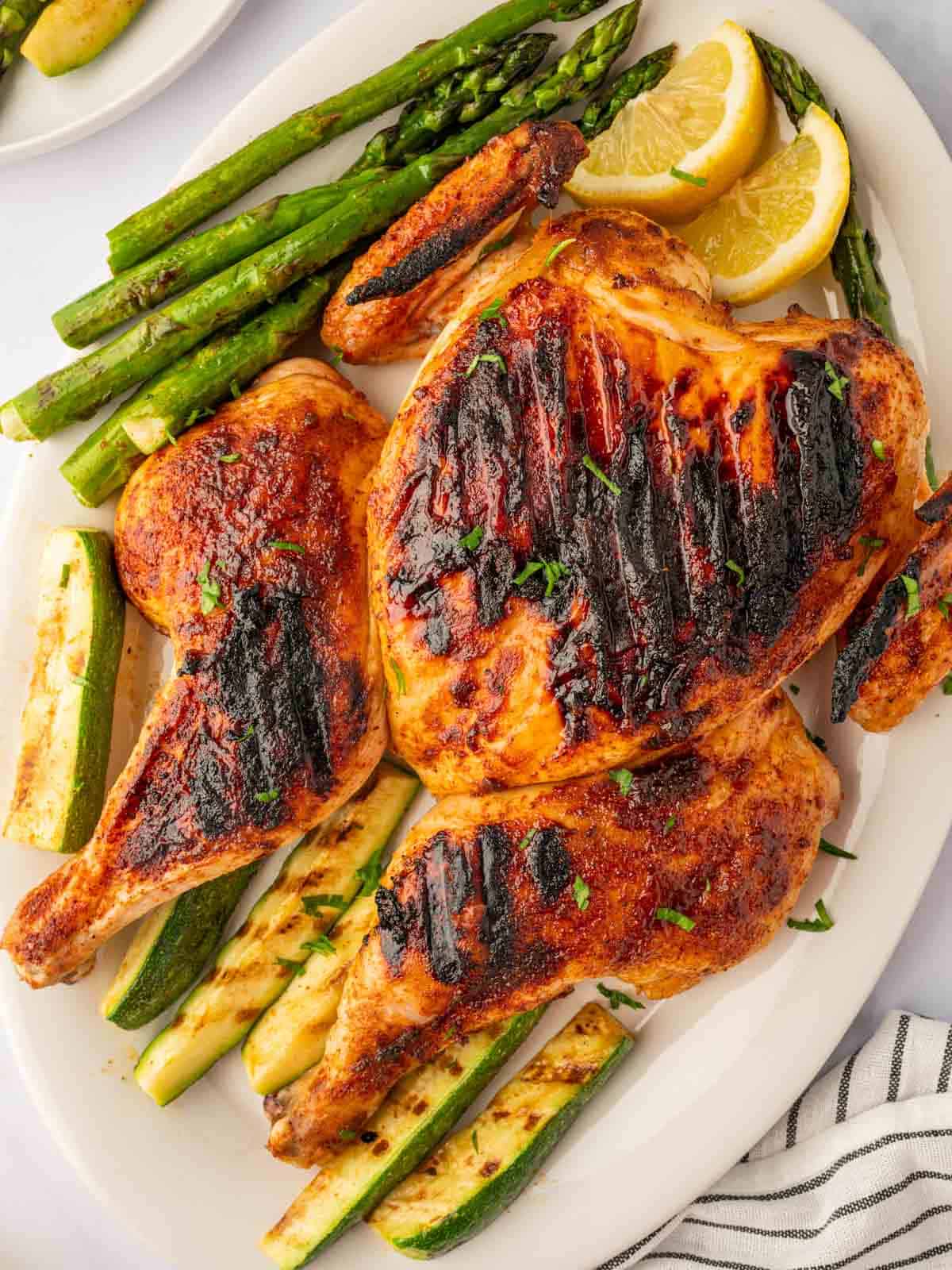 Charcoal grilled chicken on a platter with grilled vegetables.
