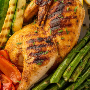 Grilled half chicken with grill marks, asparagus, zucchini, and red bell pepper.