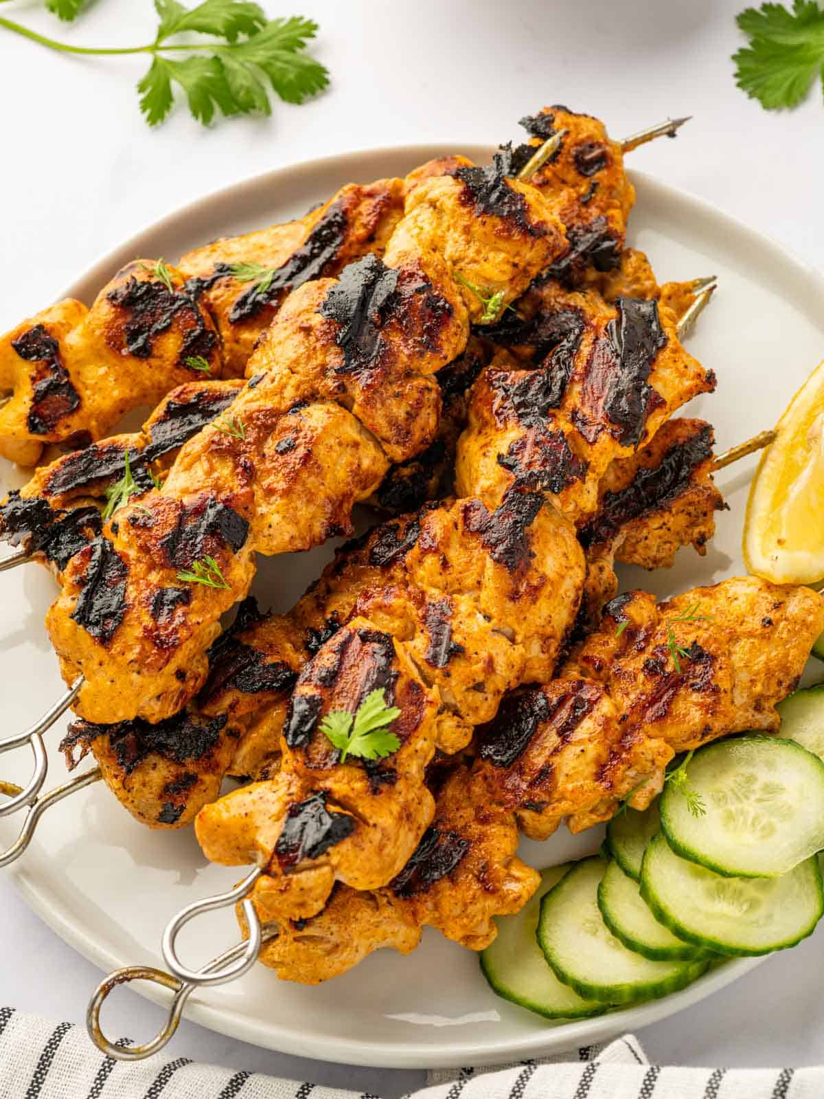 Grilled Tandoori chicken on a platter with cucumber.