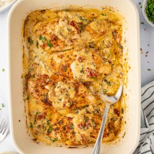 A spoon scoops tuscan sauce from the casserole dish.