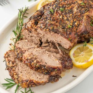 Leg of lamb with slices cut garnished with lemon and rosemary.