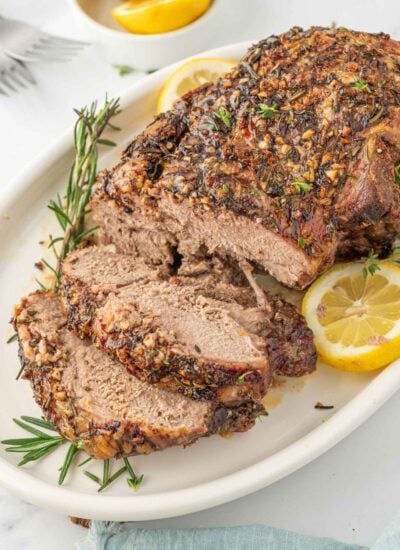 Leg of lamb with slices cut garnished with lemon and rosemary.