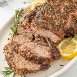Leg of lamb with slices cut garnished with lemon and rosemary.