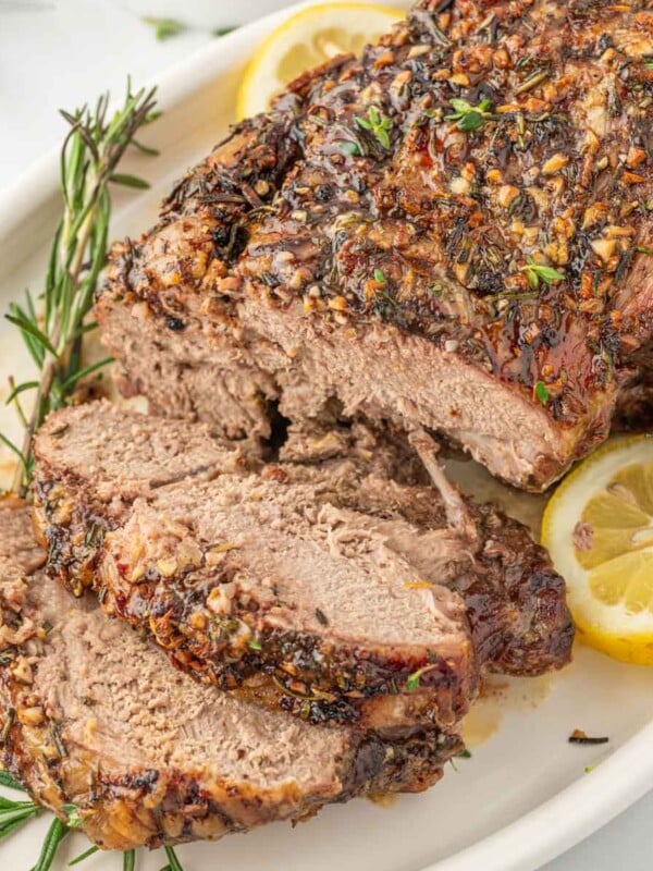 Leg of lamb with slices cut garnished with lemon and rosemary.