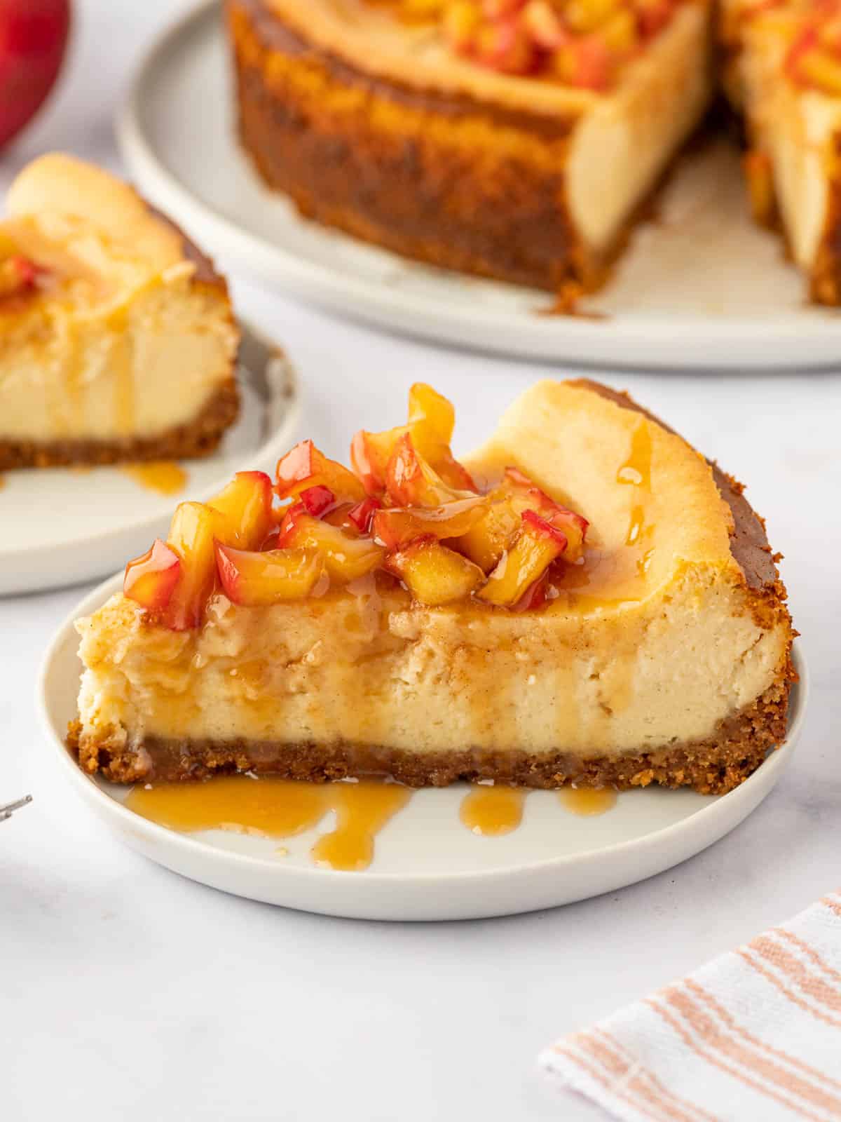 A slice of cinnamon cheesecake with apple topping rests on a plate.