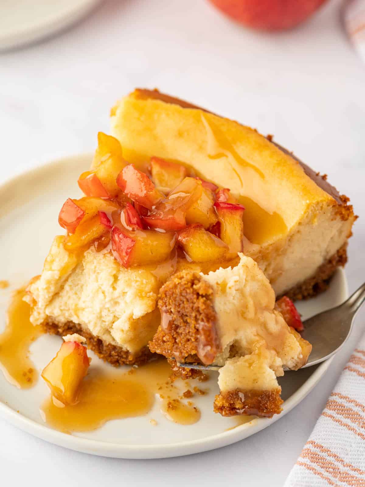 A fork cuts a bite of creamy cheesecake with apple topping.