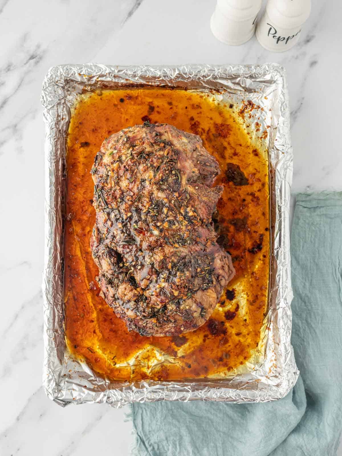 Roasted leg of lamb in its juices in a baking dish lined with foil.