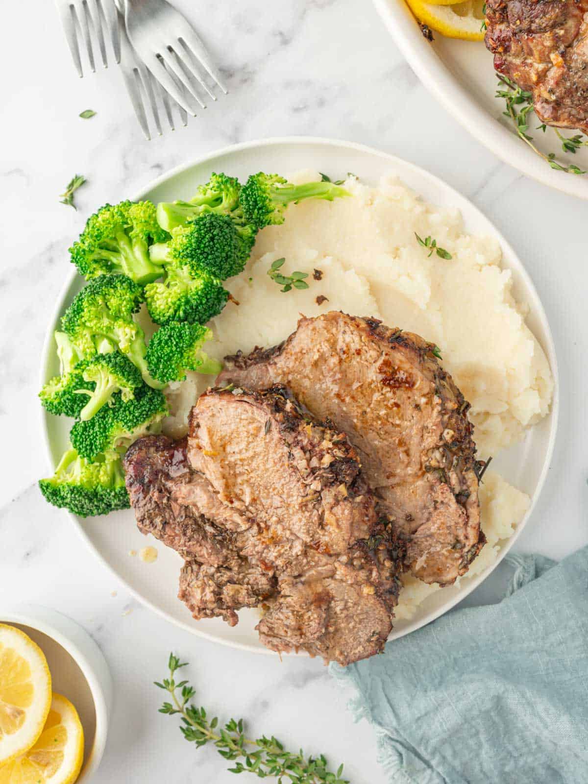 Sliced of roasted lamb on a plate with mashed potatoes and broccoli.