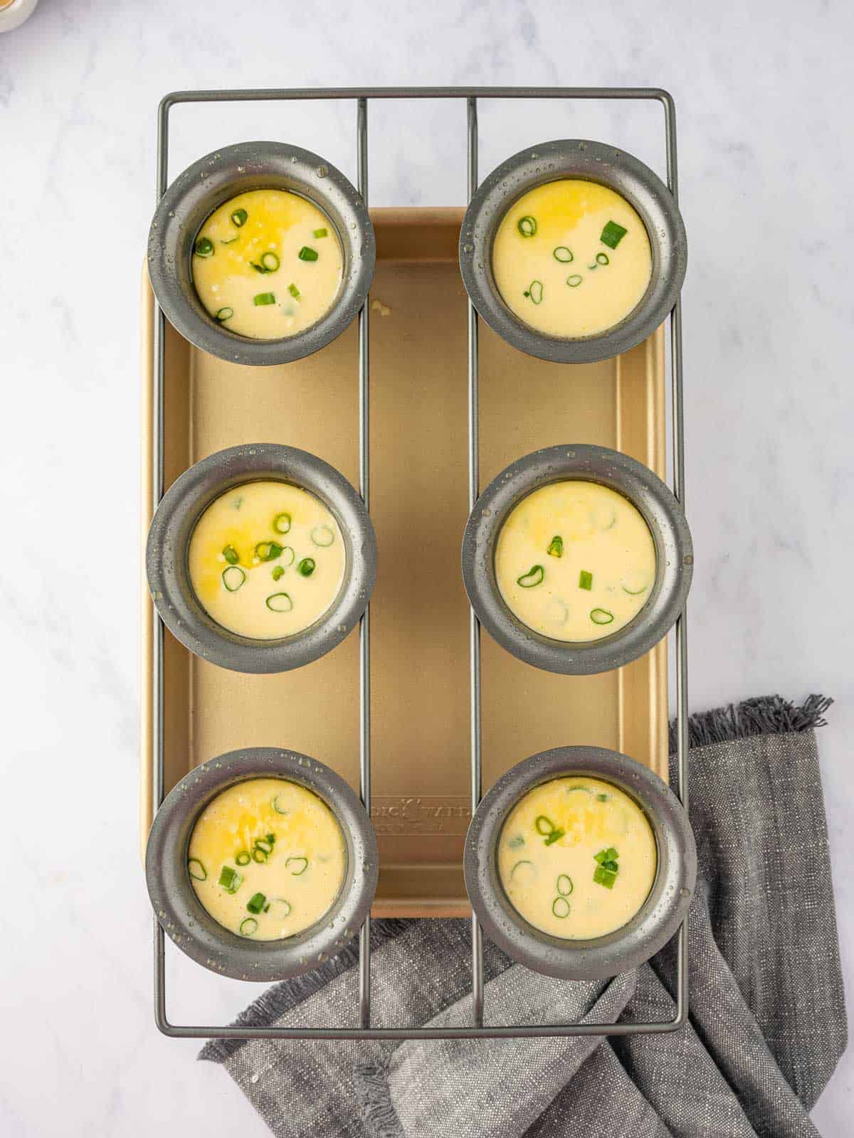 Popover batter divided among pan cups with sliced green onions.