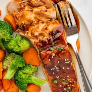 Teriyaki marinated salmon on a plate with veggies and a fork.