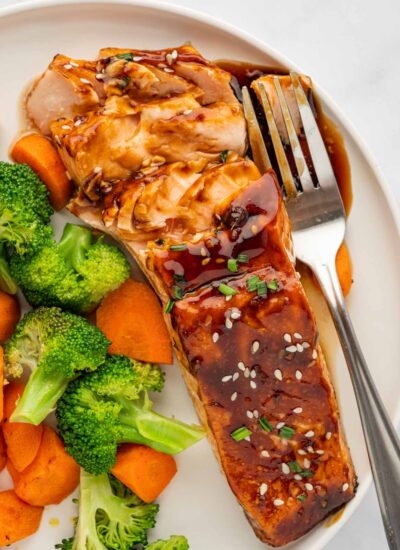 Teriyaki marinated salmon on a plate with veggies and a fork.