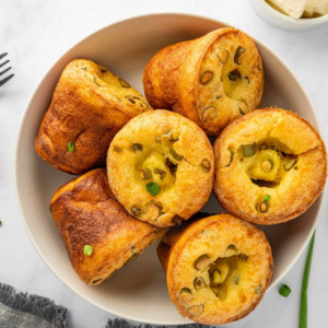Golden brown popovers with scallions arranged in a serving bowl.