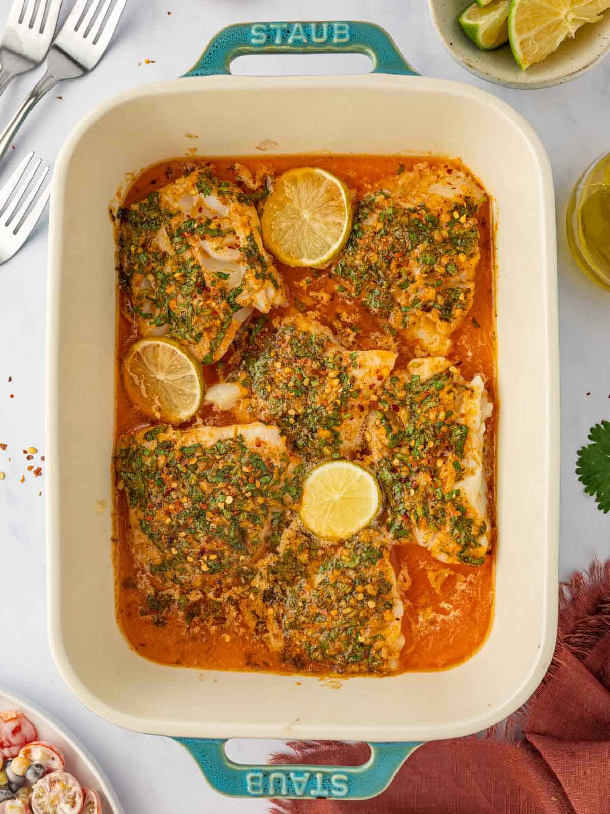 A casserole dish with herb lime baked cod topped with lime slices.