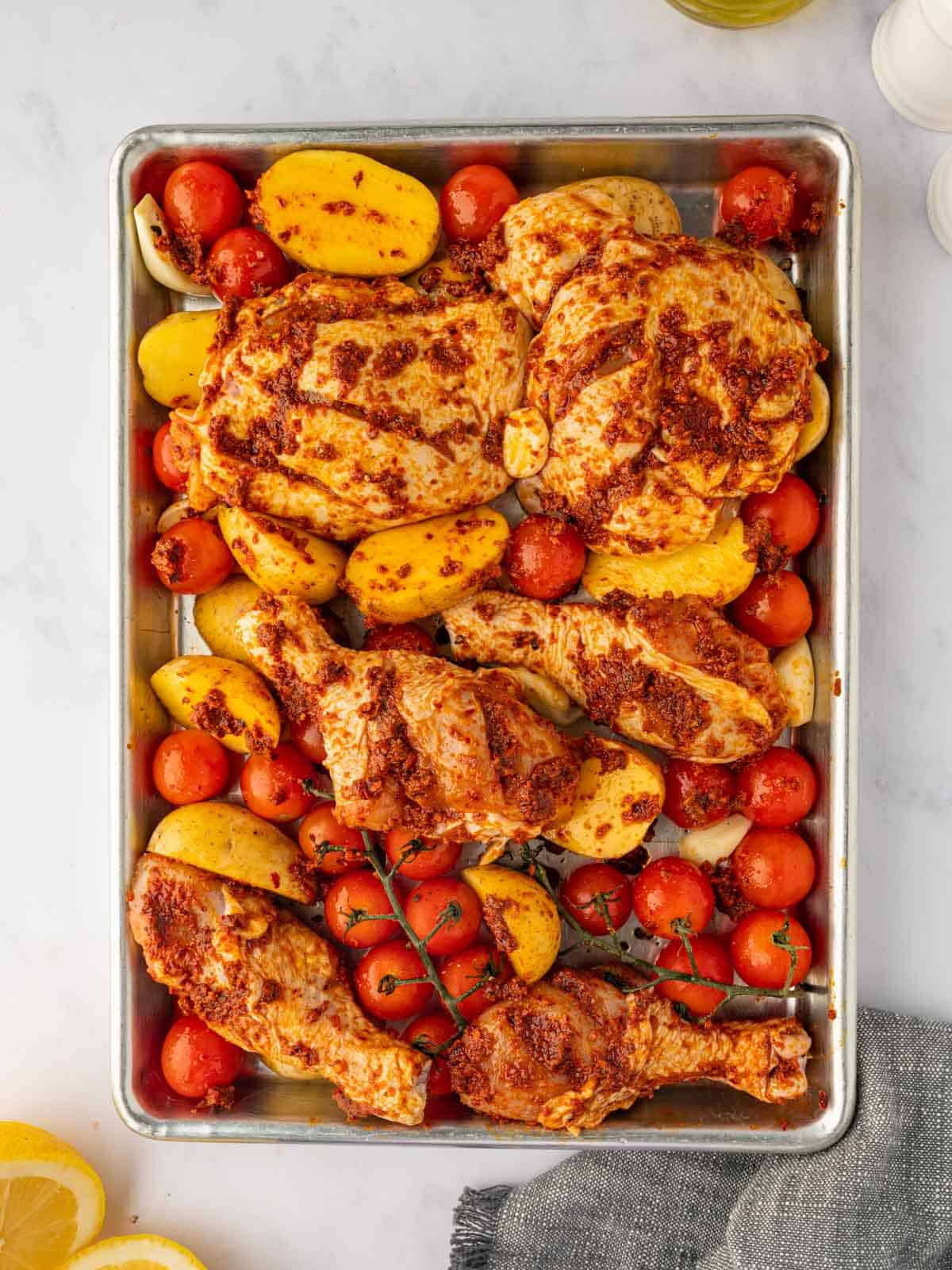 Harissa marinated chicken on a sheetpan with tomatoes and potatoes.