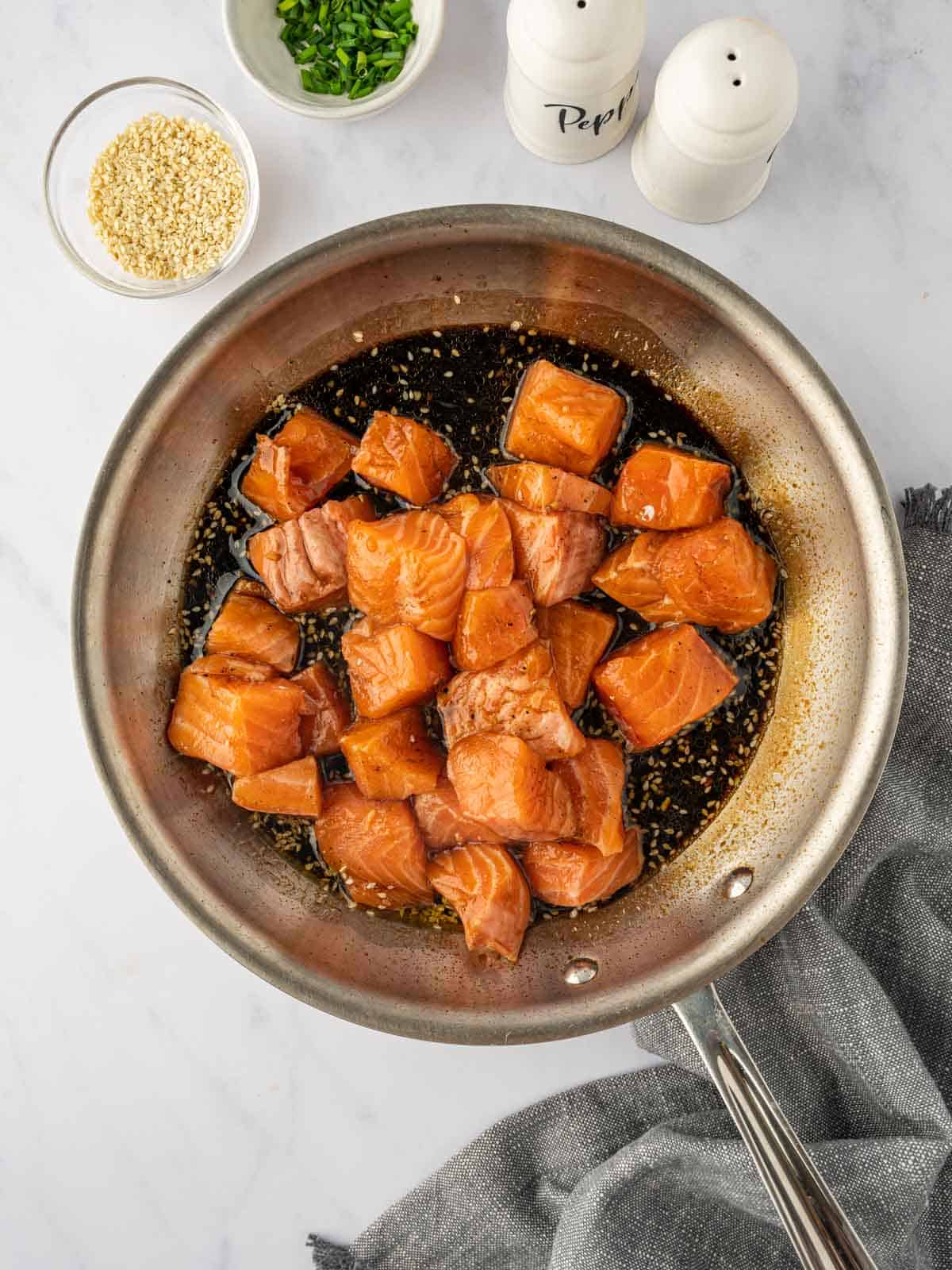 Marinated salmon cubes are cooked in a skillet.