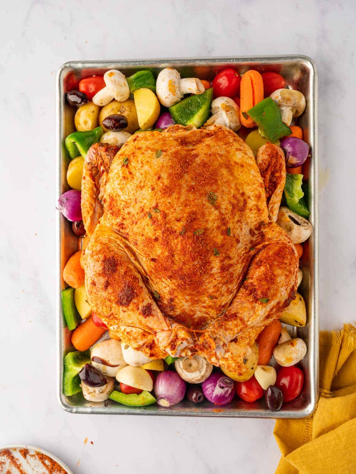 Seasoned whole chicken on a baking sheet with vegetables.