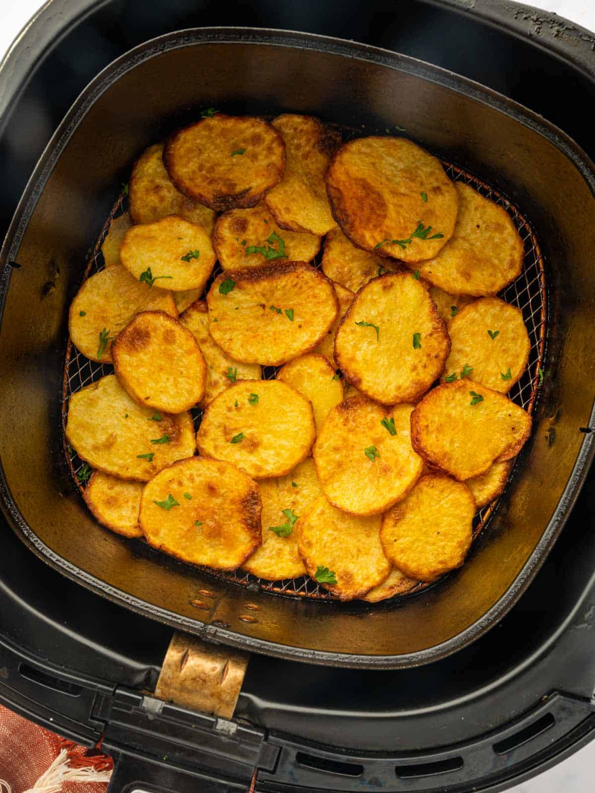 Crispy sliced potatoes in the air fryer garnished with parsley.