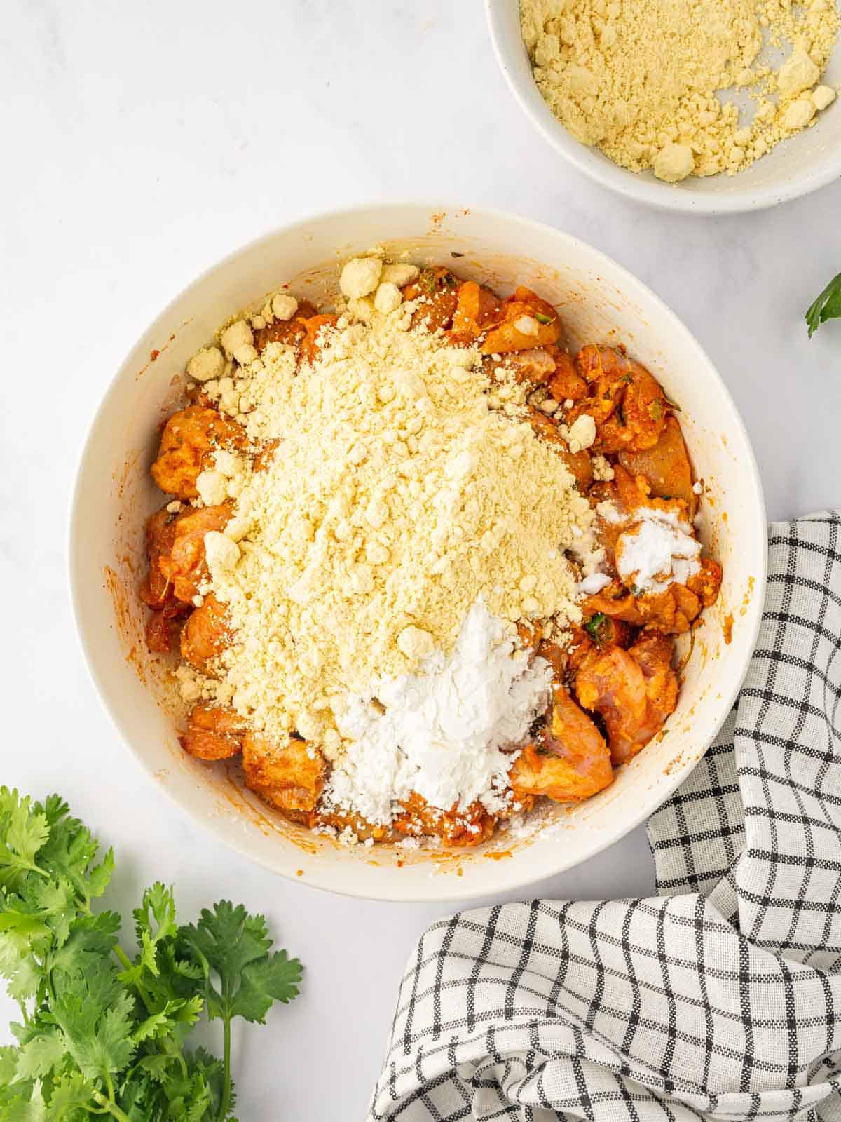 Combining marinated chicken with flour for batter in a bowl.