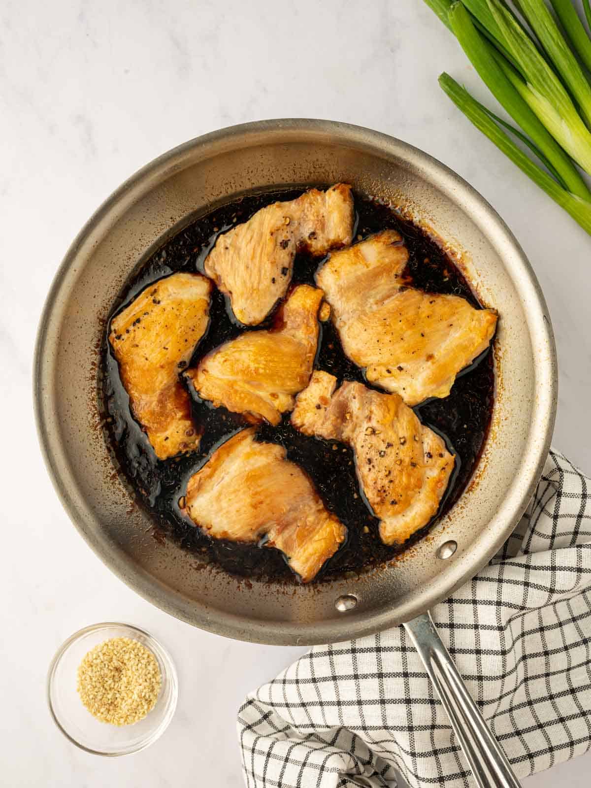 Chicken cooks in teriyaki sauce in a skillet.